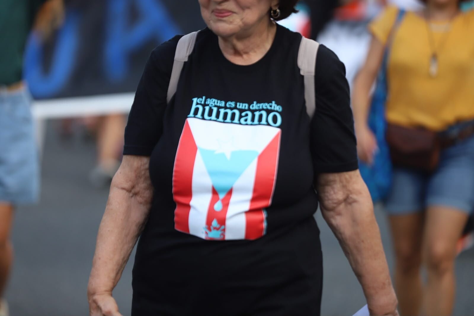 Une femme porte un t-shirt : el agua es un derecho humano, sur un drapeau portoricain.
