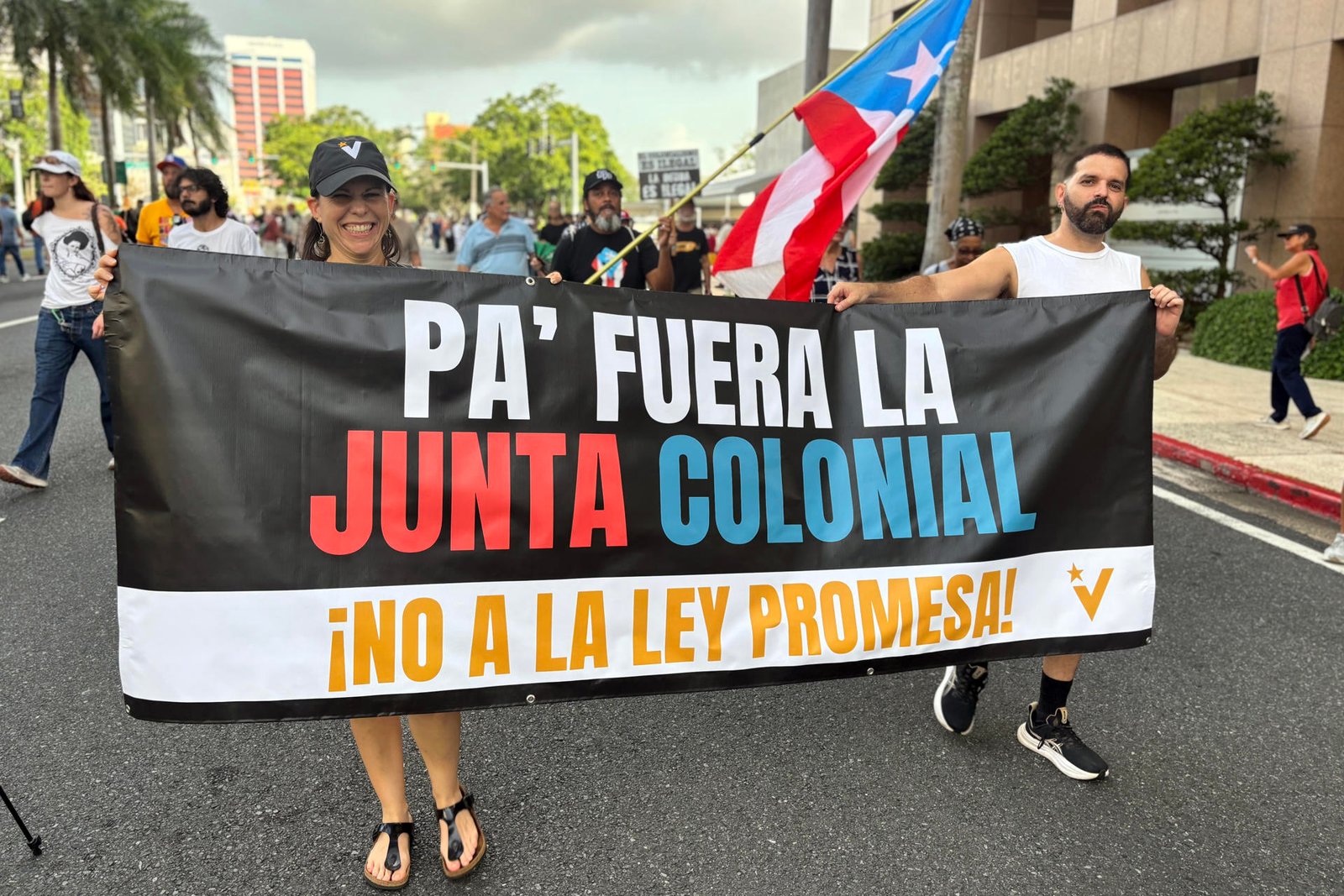 Deux personnes tiennent une banderole PA FUERA LA JUNTA COLONIAL et NO A LA LEY PROMESA.